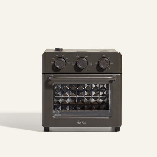 The AU - Wonder Oven is a dark gray countertop toaster oven with three top control dials and a front glass door featuring a diamond-patterned interior. "Our Place" appears at the bottom of the door. Doubles as an air fryer for extra versatility.