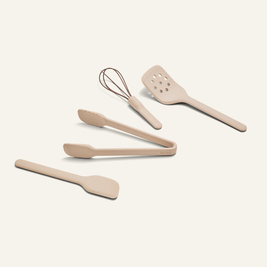 Four beige Mini Utensil Essentials—spatula, tongs, slotted turner, and whisk—are arranged on a plain light background.