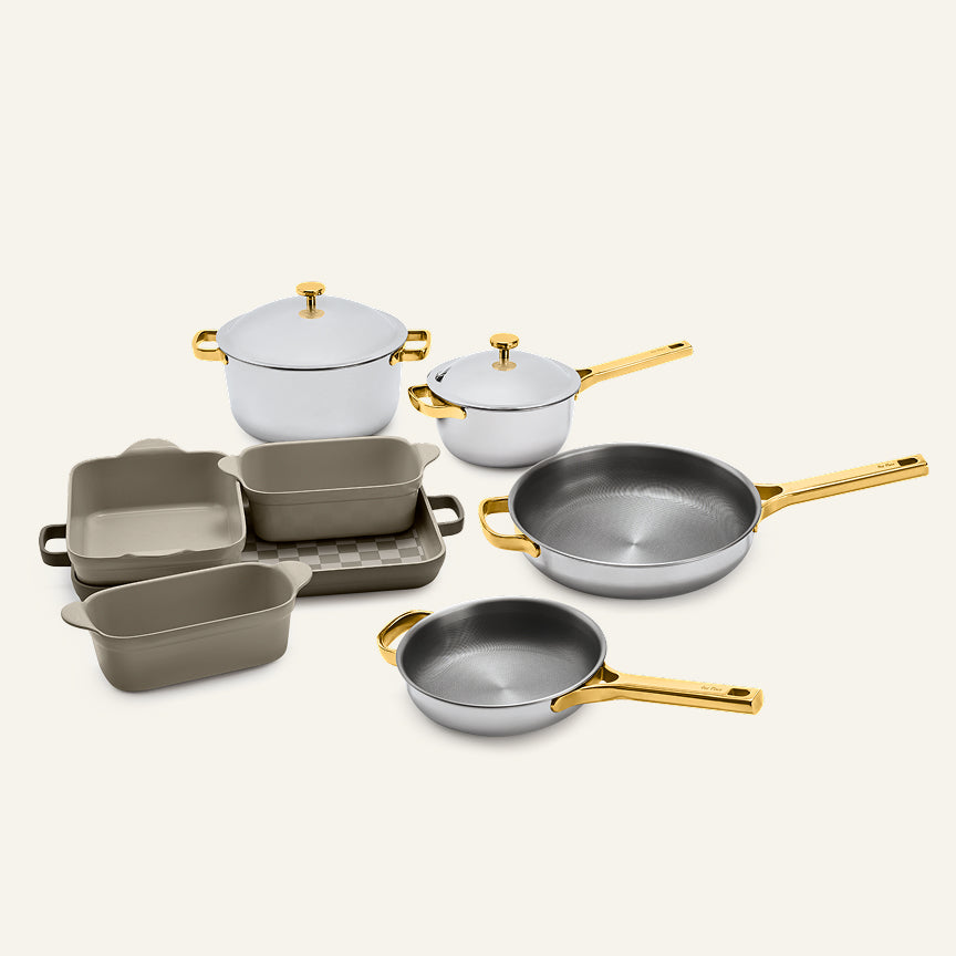 Titanium Pro Cookware + Bakeware Set 2.0 including two lidded pots, two frying pans, and three ceramic bakeware dishes with gold-toned handles and lids.