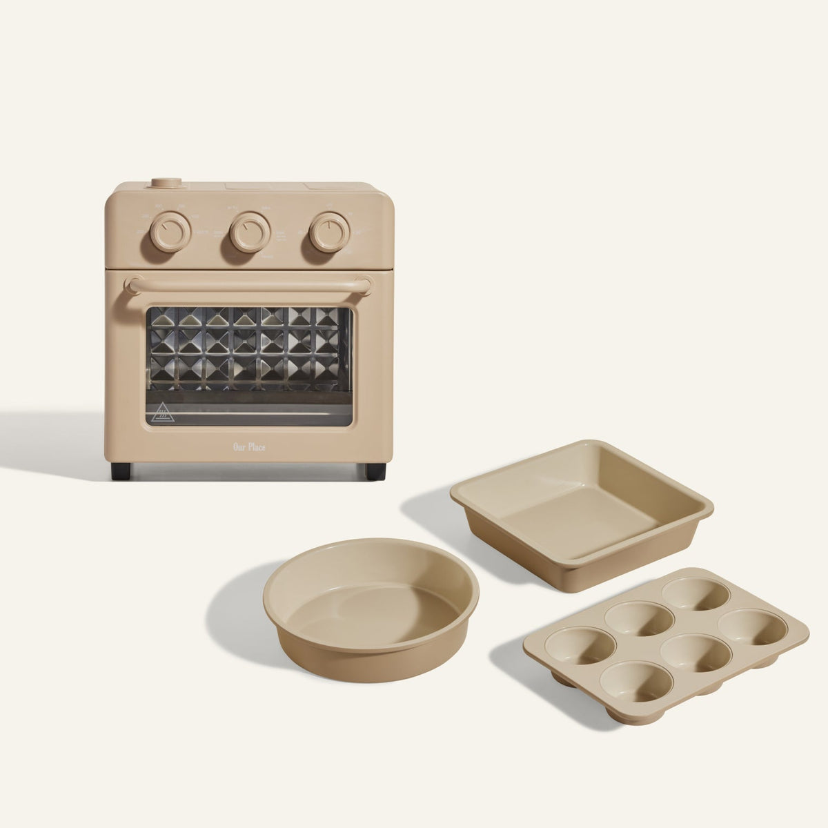 The Wonder Oven + Wonder Oven Baker's Kit is displayed in beige, featuring a countertop oven with a matching square pan, round pan, and six-cup muffin tray on a light background.
