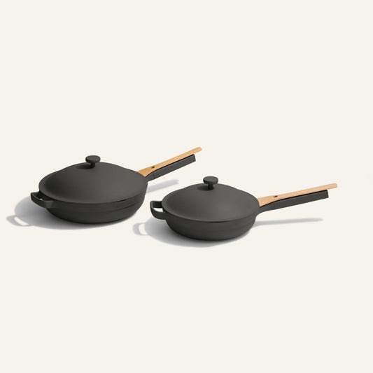 The Always Pan Duo—two black nonstick pans in different sizes, each with a matching lid and wooden handle—are displayed side by side on a light background, offering versatile cookware inspired by the iconic Always Pan.