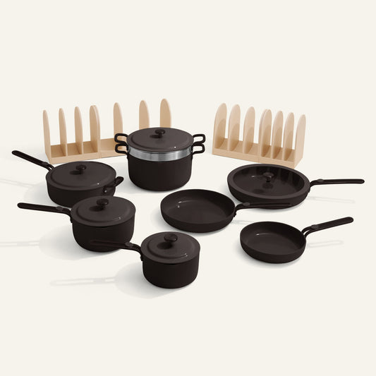 Set of black cookware with lids and wooden racks on a white background