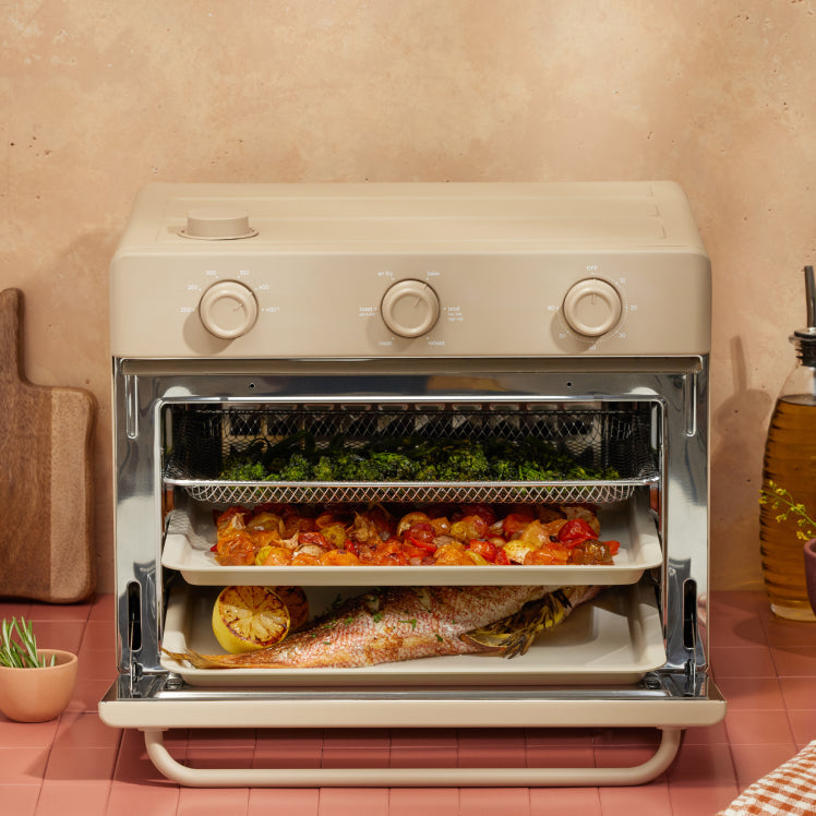 cooking vegetables, and fish on three trays in beige large wonder oven non toxic air fryer toaster oven on counter