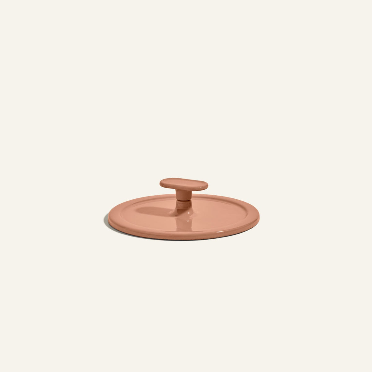 A terracotta-colored, round ceramic lid with a central handle—resembling the Grill Press—is displayed against a plain light background, highlighting its even heat distribution.