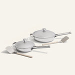 Set of white cookware with lids and wooden spatulas on a light gray background